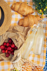A small picnic with croissants, strawberries, and lemonade on an orange checkered blanket
