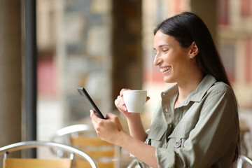 Happy woman drinks coffee in a bar using phone