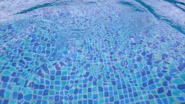 Water ripples on blue tiled swimming pool during rain.  Falling raindrops on the water surface of a blue pool, rainy day at a hotel while traveling in southeast Asia. Monsoon and rainy season
