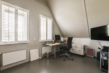 a home office with white shutters on the windows, and a computer desk in front of a large window