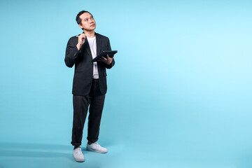 Full length portrait of Asian man using tablet computer looking up to copy space over blue background