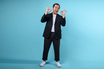 Full body portrait of an adult man in formal wear giving okay hand gesture isolated over blue background.