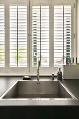 a kitchen sink and window with plantation shutters in the window behind it, which is open to let...
