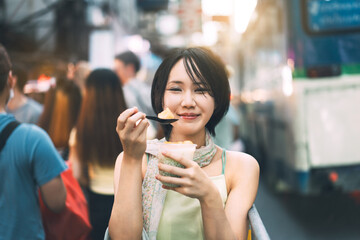 Young adult asian foodie woman eating thai dessert at china town street food