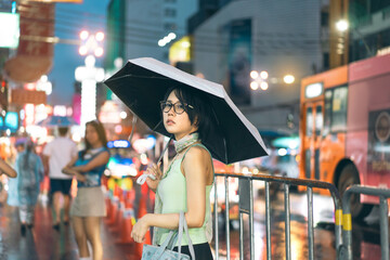Asian woman wear y2k nostalgia trend outfit using umbrella rainy season at chinatown on night city