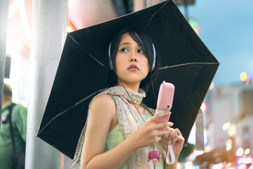 Asian woman wear nostalgia stylish using headphone and flip phone with umbrella on rainy season at...
