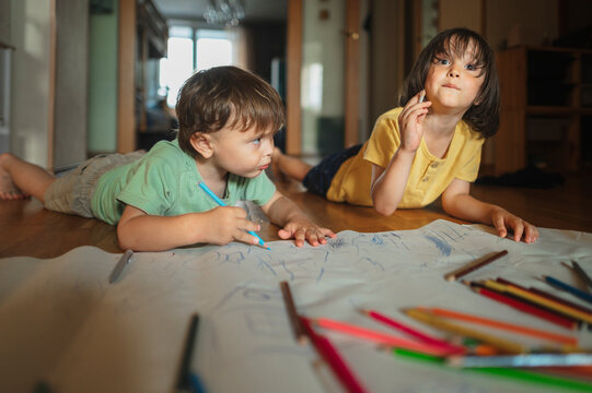 Brothers drawing with colored pencils lying on floor at home