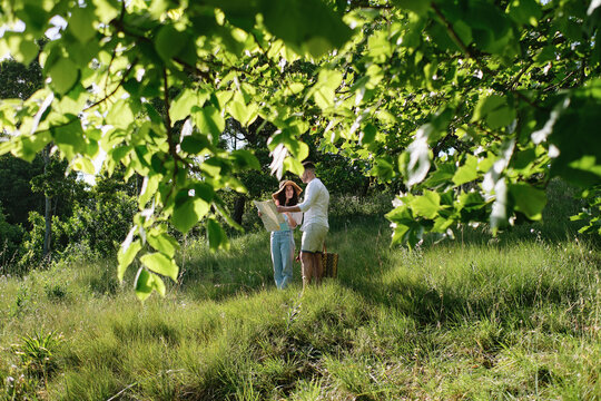 Couple discussing over map standing on grass in park at sunny day