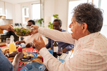 Senior man passing salad bowl to friend at home