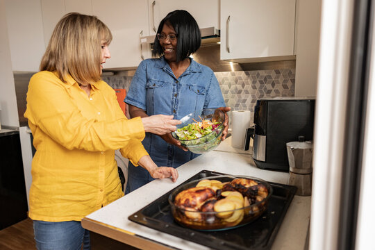 Senior woman assisting friend preparing food in kitchen at home