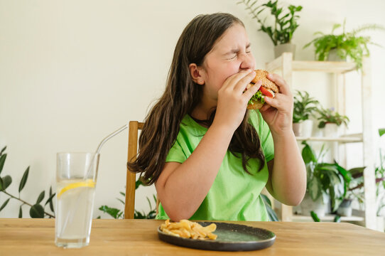 Girl eating hamburger with french fries and soda at home