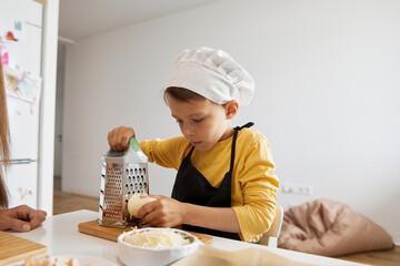 Boy grating cheese with grater in kitchen at home