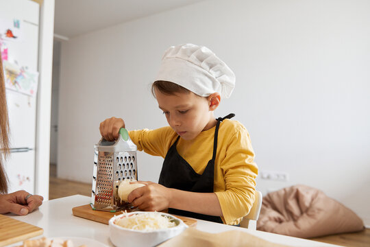 Boy grating cheese with grater in kitchen at home