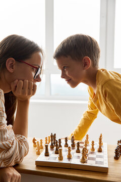 Smiling boy looking and playing chess with mother at home