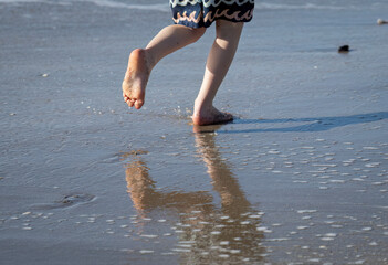 Beautiful legs of a young child running on a beach with reflection on the wet sand.