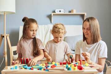 Obraz na płótnie Canvas Happy childhood memories. Imaginative play sessions. Educational toy collection. Parental teaching moments. Charming children playing together with mother with wooden sorter toys at home interior.