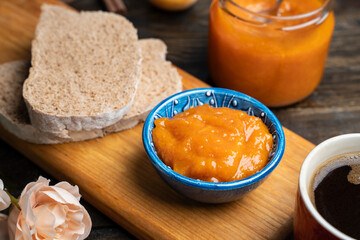Apricot jam in a blue ceramic bowl, bread and fresh apricots on a wooden background