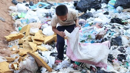 A poor boy collecting garbage waste from a landfill site in the outskirts . children work at these sites to earn their livelihood. Poverty concept.