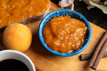 Apricot jam in a blue ceramic bowl, bread and fresh apricots on a wooden background