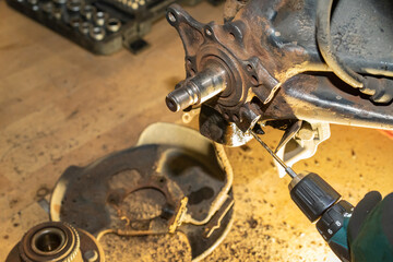 The car mechanic drills a thread. Repair wheel hub bearing. Workshop. Yellow light. - obrazy, fototapety, plakaty