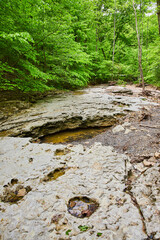 Dried up riverbed with limestone rocks and tiny pool of water in lush green forest