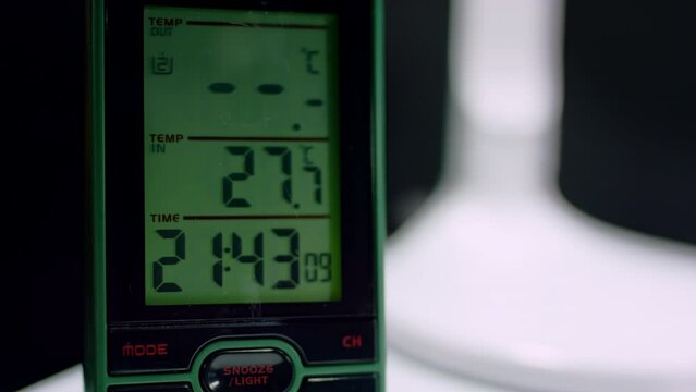 Green digital clock shows 21:43 time at darkness. Electronic clock stands on table in study room showing time and temperature