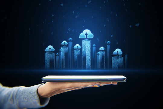 Metaverse and cloud technology concept with blue glowing city skyscrapers visualization with cloud icons above digital tablet in human hand on dark background