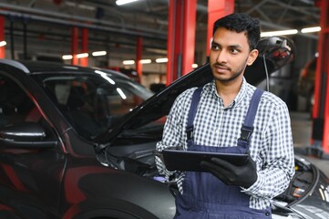 Mechanic man mechanic manager worker using a laptop computer checking car in workshop at auto car repair service center. Engineer young man looking at inspection vehicle details under car hood.