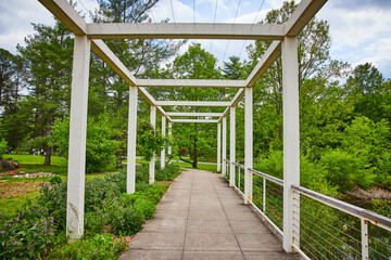 White pergola next to pond with flowers on side of path and park trails