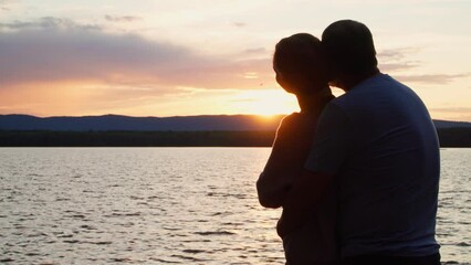 A couple in love stands on the shore of the lake at sunset and admires nature. Romantic relationships and harmony with nature.