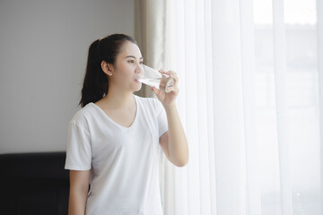 Healthy beautiful Asian young woman drinking pure water from glass at home. Caucasian female model holding transparent glass. Healthy eating woman concept.