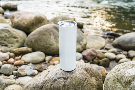 Nature's enchanting allure comes alive in this captivating mockup image, featuring a white blank long wine tumbler gracefully placed by a flowing river