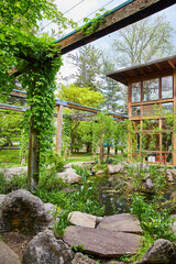 Vertical of gorgeous pond with natural elements and vine covered pergola leading to two story cabin
