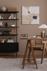 Warm and cozy office interior with mock up poster frame, wooden desk, rattan chair, books, black rack, stylish lamp, vase with branch, books, brown wall and personal accessories. Home decor. Template.