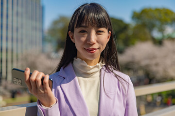 A portrait of Japanese woman with smartphone behind cherry blossom bust shot