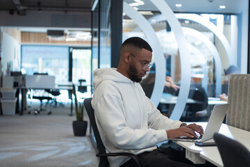 In a modern office setting, an African American businessman is diligently working on his laptop,...