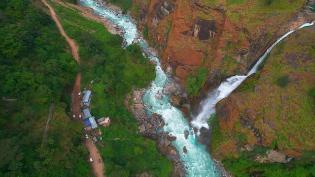 Aerial establishing shot tourist by Chyamche waterfall with house settlement.Annapurna circuit trek way to Manang. Nepals Himalayas famous sightseeing trekking destination.