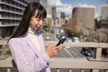 A portrait of Japanese woman using smartphone behind cherry blossom