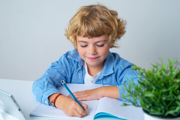 Primary school smiling boy girl sitting at desk, studying alphabet writing letter book and tablet...
