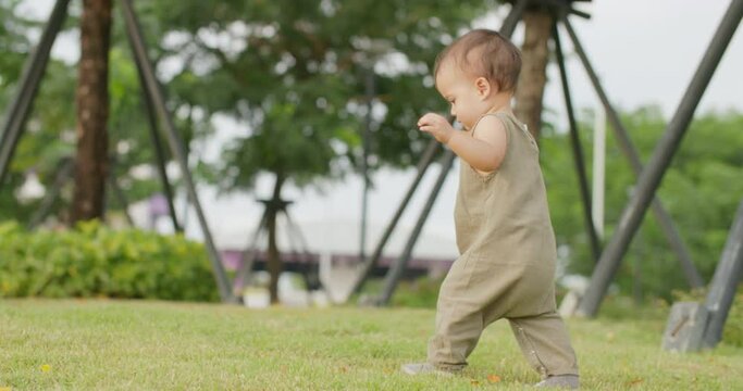 Adorable little happy smiling kid playing in the park. Cute baby girl walks on green grass in summer vacation. Active caucasian child learning to walk in outdoor nature on sunny spring day. Slow Motio