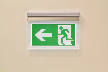 Close-up of green emergency exit sign showing the way to escape on wall. Fire exit in corridor of...