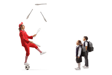 Children watching a man in a red suit standing on a ball and juggling