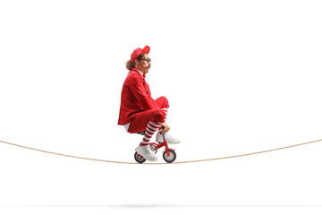 Man in a red suit riding a small red bike on a rope