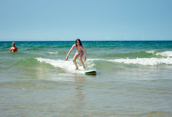 Pretty young girl sliding on ocean waves with her surfboard