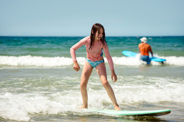 Pretty young girl sliding on ocean waves with her surfboard