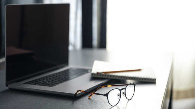 Laptop, glasses and notebok on the desktop on a blurred background.