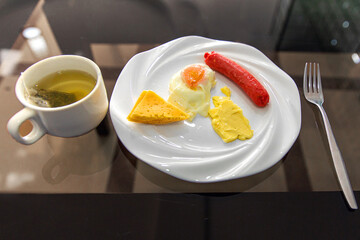 Delicious appetizing tomorrow - scrambled eggs with butter, cheese and sausage. Green tea in a cup