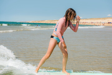 Pretty young girl sliding on ocean waves with her surfboard