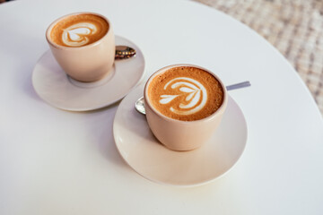 Two cups of cappuccino on a white table in an outdoor cafe 