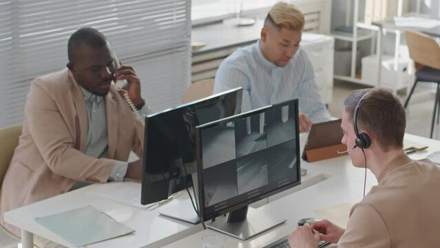 Slowmo of three multiracial security service managers coworking in agency, monitoring CCTV cameras and making phone calls